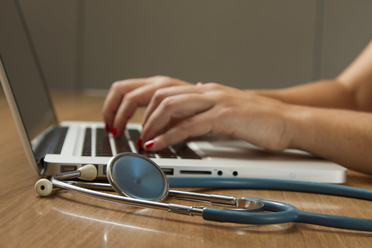 Hands typing on a laptop next to a stethoscope